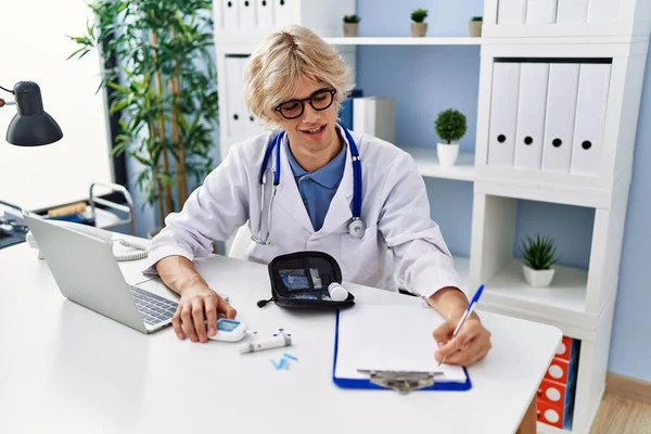 Młody Blondynka Mężczyzna Lekarz Uśmiechając Pewny Siebie Pisanie Dokumencie Klinice — Zdjęcie stockowe