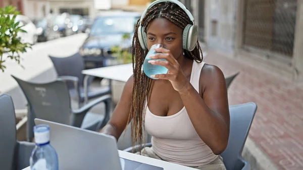 Mujer Afroamericana Usando Laptop Auriculares Bebiendo Vaso Agua Terraza Cafetería — Foto de Stock