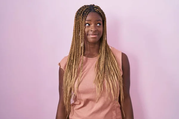 Африканская Американка Плетеными Волосами Стоящая Розовом Фоне Улыбаясь Смотрит Сторону — стоковое фото
