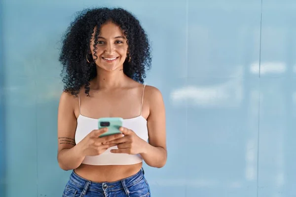 stock image Young hispanic woman smiling confident using smartphone over blue background