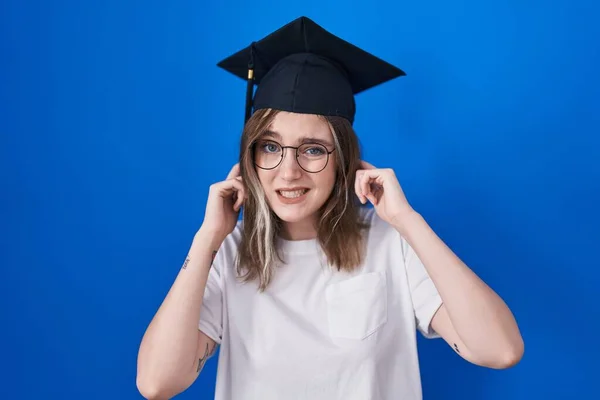大音量の音楽のノイズのためにいらいらする表情で指で耳を覆う卒業キャップを身に着けているブロンドの白人女性 聴覚障害の概念 — ストック写真