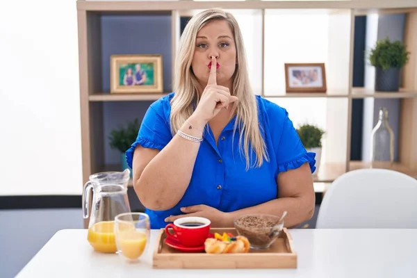 コーカサスとサイズの女性は 唇に指で静かにするように頼んで自宅で朝食を食べます 沈黙と秘密の概念 — ストック写真