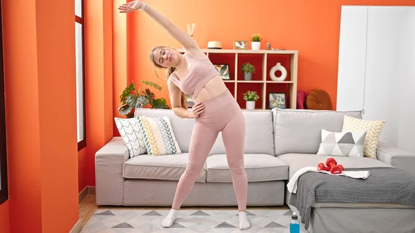 Młoda Blondynka Ubrana Odzież Sportową Rozciągająca Się Domu — Zdjęcie stockowe