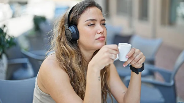 若い美しいヒスパニック系の女性がコーヒーショップテラスでコーヒーを飲む音楽を聞いて ストック写真