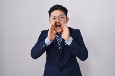 Genç Asyalı takım elbiseli ve kravatlı adam elleri ağızda bağırarak bağırıyor. 