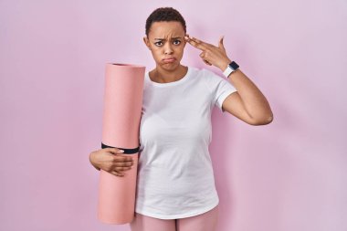Güzel Afrikalı Amerikalı kadın yoga minderini tutuyor ve kendini vuruyor ve öldürüyor. Kendini ve parmaklarını silah gibi gösteriyor. İntihar jesti.. 