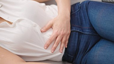 Orta yaşlı İspanyol kadın adet sancısı çekiyor. Evdeki kanepede yatıyor.