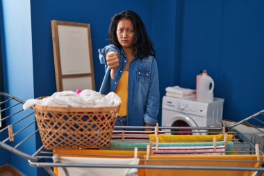Çamaşır ipine kıyafet asan genç Asyalı kadın mutsuz ve kızgın görünüyor. Reddedilmiş ve olumsuz hareketler yapıyor. kötü ifade. 