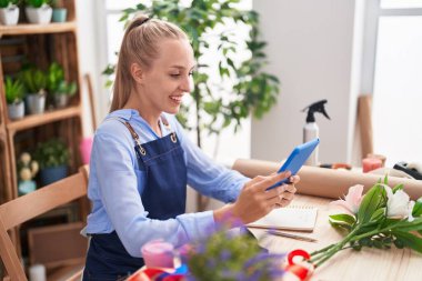 Young blonde woman florist smiling confident using touchpad at florist