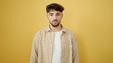 İzole edilmiş sarı arka planda gevşek bir ifadeyle duran genç bir Arap.