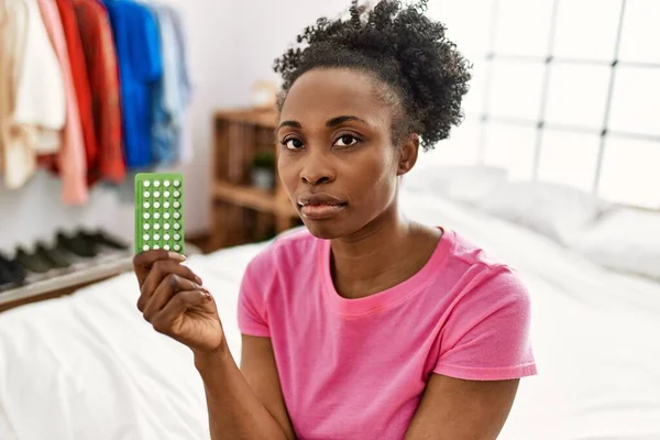 非洲裔美国妇女坐在卧室的床上 手里拿着避孕药 — 图库照片