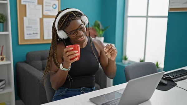 アフリカ系アメリカ人女性ビジネスワーカーが音楽を聴きながらオフィスでコーヒーを飲みながら踊る — ストック写真