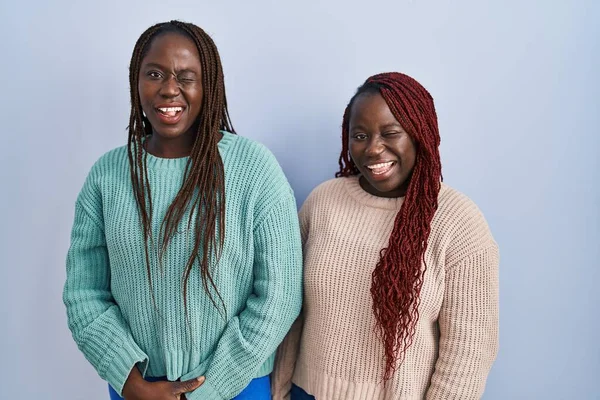 二つのアフリカの女性立ちます上の青の背景ウィンク見ますザ カメラとともにセクシー式 陽気で幸せな顔 — ストック写真