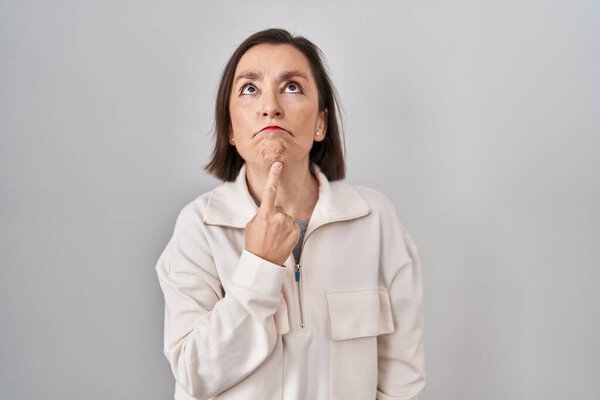 Middle age hispanic woman standing over isolated background thinking concentrated about doubt with finger on chin and looking up wondering 