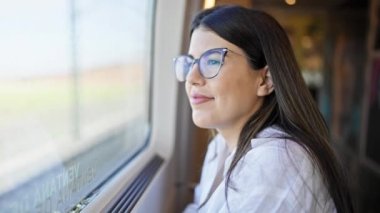 Genç ve güzel İspanyol kadın, tren istasyonunun penceresinden bakıp mutlu bir şekilde gülümsüyor.