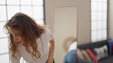 Genç bir kadın aynaya bakıyor. Evde ceket giyiyor.