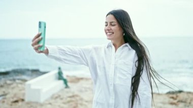 Genç, güzel, İspanyol bir kadın deniz kenarında öpüşen akıllı telefonun yanında selfie çekiyor.