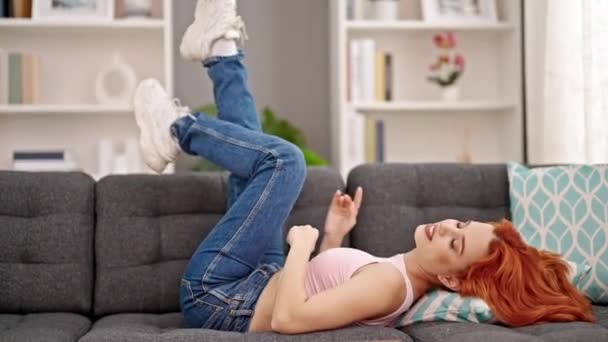 年轻的红头发女人躺在沙发上 在家里跳舞 — 图库视频影像