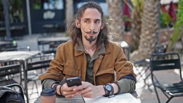 喫茶店のテラスを見ているスマートフォンを使用して若いヒスパニック系男性観光客 — ストック動画
