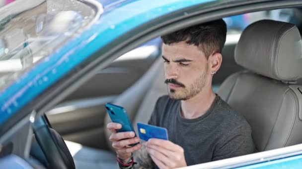 路上で車の上に座っているスマートフォンやクレジットカードを使用して若いヒスパニック系の男 — ストック動画