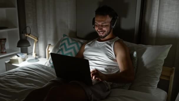 Jovem Árabe Homem Usando Laptop Sentado Cama Usando Fones Ouvido — Vídeo de Stock
