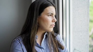 Genç, güzel, İspanyol bir kadın evde üzgün bir ifadeyle pencereden dışarı bakıyor.