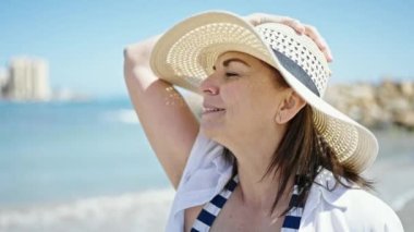 Orta yaşlı İspanyol turist. Kumsalda elinde şapkayla gülümsüyor.