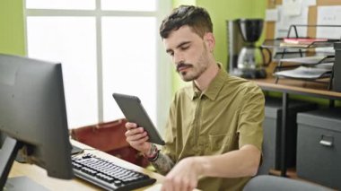 Young hispanic man business worker using touchpad writing on document at office