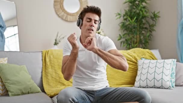 Молодой Латиноамериканец Слушает Музыку Сидя Дома Диване Танцуя — стоковое видео