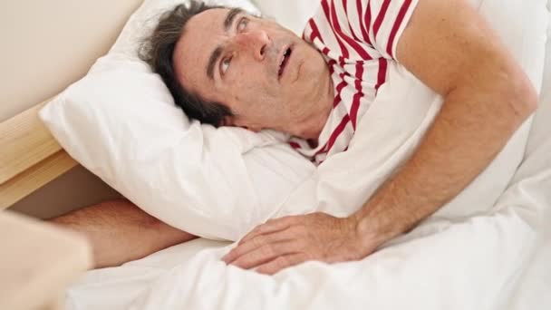 寝室のベッドに横たわる騒音のために耳を覆う中年男性 — ストック動画