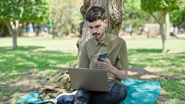 Młody Latynos Człowiek Pomocą Laptopa Rozmowy Smartfonie Parku — Wideo stockowe
