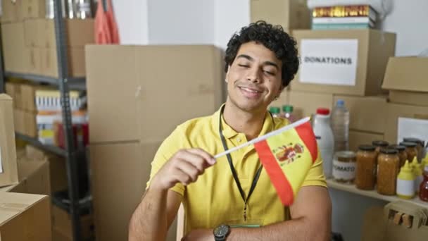チャリティーセンターで笑顔のスペイン国旗を掲げた若いラテン系男性ボランティア — ストック動画