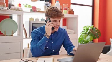 Laptop ve kredi kartıyla alışveriş yapan İspanyol genç yemek odasında akıllı telefondan konuşuyor.