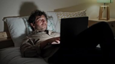 Genç İspanyol adam yatak odasında çalışırken dizüstü bilgisayar kullanıyor.