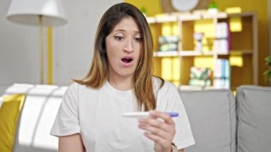 Evde endişeli bir ifadeyle hamilelik testi tutan genç sarışın kadın.