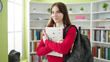 Genç İspanyol kız öğrenci gülümsüyor. Kütüphanede laptopa sarılıyor.