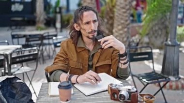 Genç İspanyol turist akıllı telefonuyla sesli mesaj yolluyor kahve dükkanının terasında oturuyor.