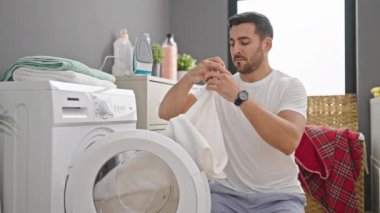 Genç İspanyol adam gülümsüyor. Çamaşırhanede yüzüyle kıyafetlere dokunuyor.