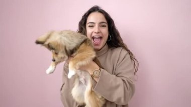 Köpeğiyle gülümseyen, kendine güvenen, soyutlanmış pembe arka planda dans eden genç İspanyol kadın.