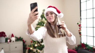 Genç ve güzel İspanyol kadın akıllı telefonuyla video görüşmesi yapıyor. Yılbaşı ağacının yanında duruyor.