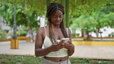 Parkta gülümseyen akıllı telefon kullanan Afrikalı Amerikalı kadın.