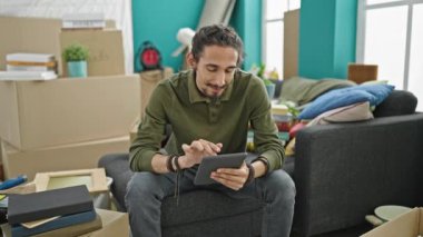 Yeni evindeki koltukta oturan dokunmatik ped kullanan İspanyol genç adam.