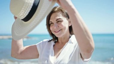 Orta yaşlı İspanyol turist. Kumsalda elinde şapkayla gülümsüyor.