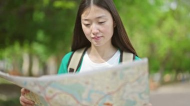 Sırt çantalı genç Çinli kadın turist parktaki şehir haritasına bakıyor.