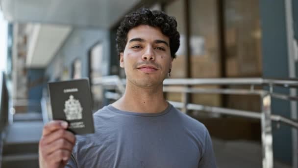 Joven Latino Sonriendo Confiado Sosteniendo Pasaporte Canadiense Calle — Vídeos de Stock