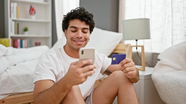 年轻的拉丁男人 拿着智能手机和信用卡坐在卧室的地板上购物 — 图库视频影像