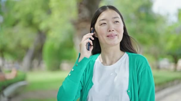 若いです中国人女性話して上のスマートフォン笑顔で公園 — ストック動画