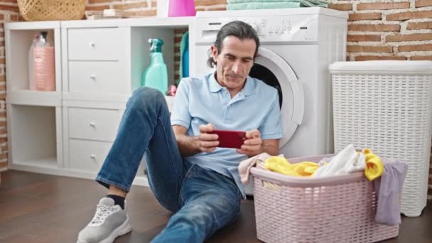 中年男子在洗衣房玩电子游戏等洗衣机庆祝 — 图库视频影像