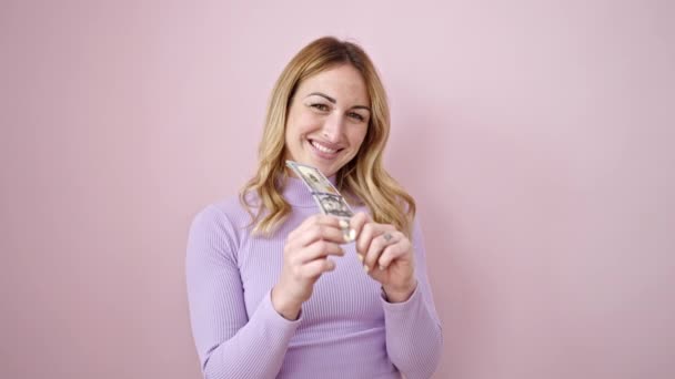 年轻而美丽的惊慌失措的女人微笑着 自信地拿着美元支撑着孤零零的粉色背景 — 图库视频影像