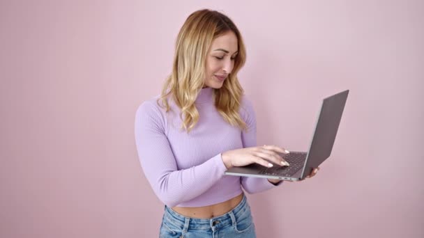年轻美丽的惊慌失措的女人带着自信地笑着 用笔记本电脑遮住了孤立的粉色背景 — 图库视频影像